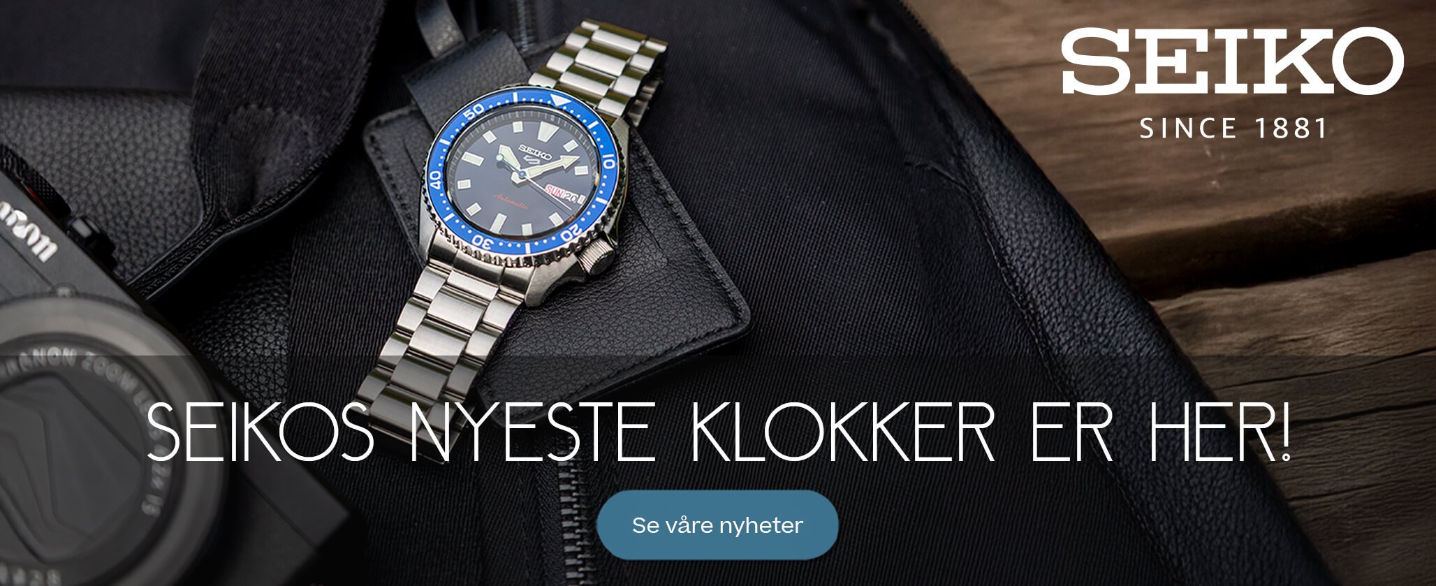 Reklamebilde for Seiko med en klokke med blå bezel og metalllenke, liggende på en svart veske med teksten «Tid for nyheter: Seikos nyeste klokker er her!».