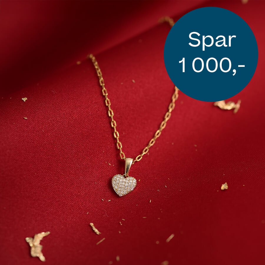 Gullkjede med hjerteanheng besatt med små diamanter ligger på rødt stoff, med blå sirkeltekst som viser «Spar 1 000,-».