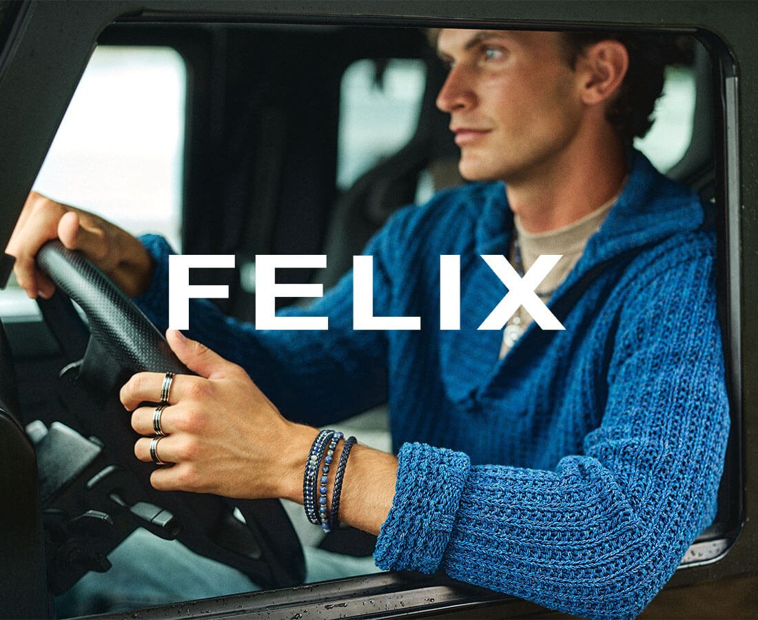 Mann med blå genser sitter bak rattet i en bil og viser smykker fra Felix-kolleksjonen med ringer og armbånd i fokus.