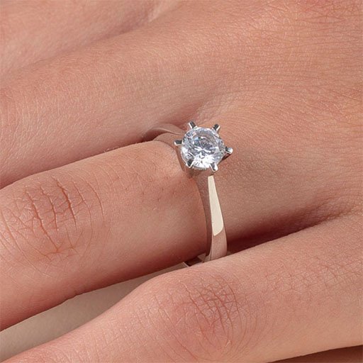 Nærbilde av en kvinnehånd, tett på ringfingeren som har en forlovelsesring i gull på seg, med en diamant holdt på plass med gull kroker.