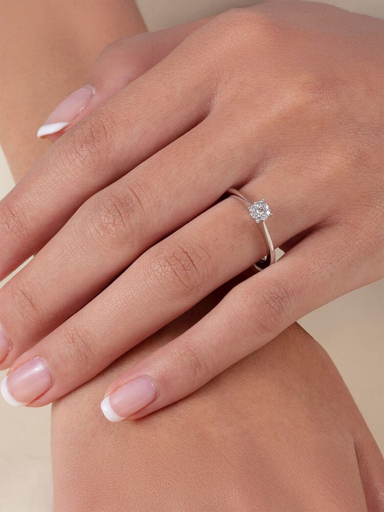 Hånd med fransk manikyr som bærer en enkel sølvring med en liten diamant på ringfingeren.