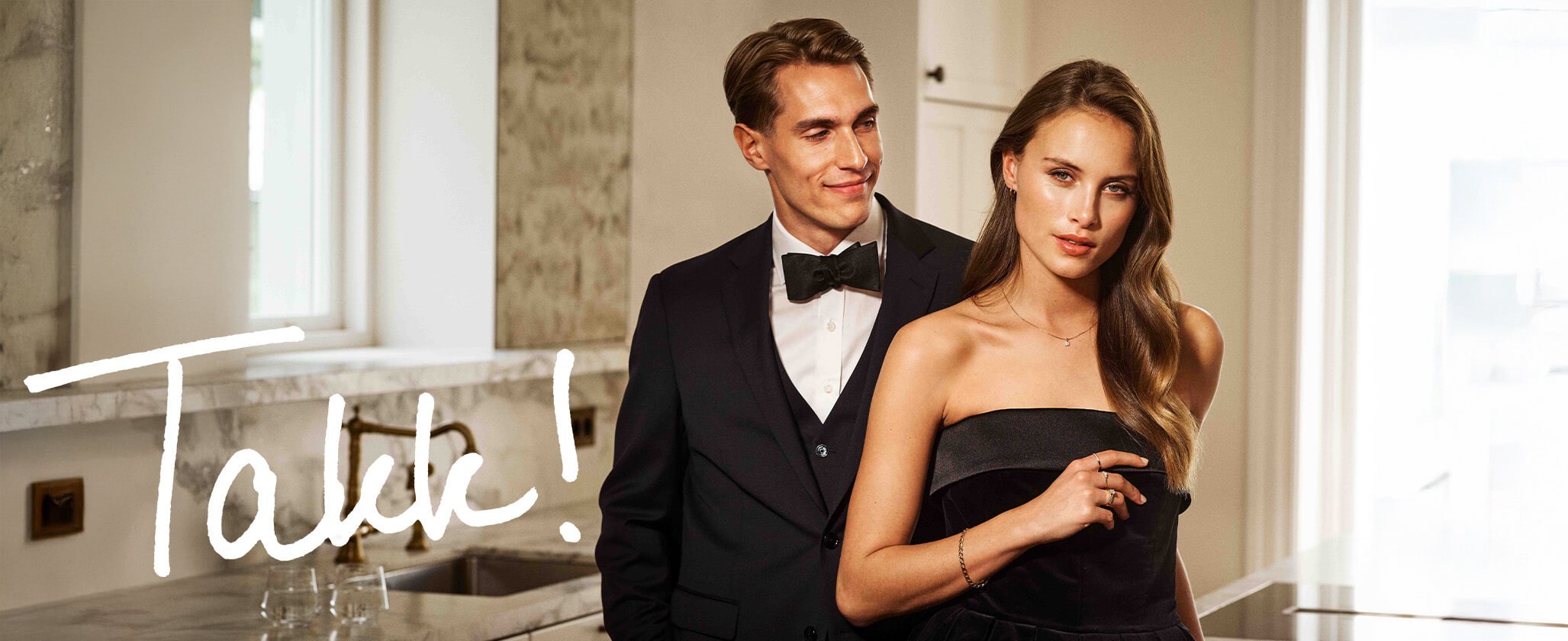 Gavekonseptet Ungt vakker par i pent antrekk. Mannen smiler og ser på kvinnen, mens kvinnen ser lystent i kamera.