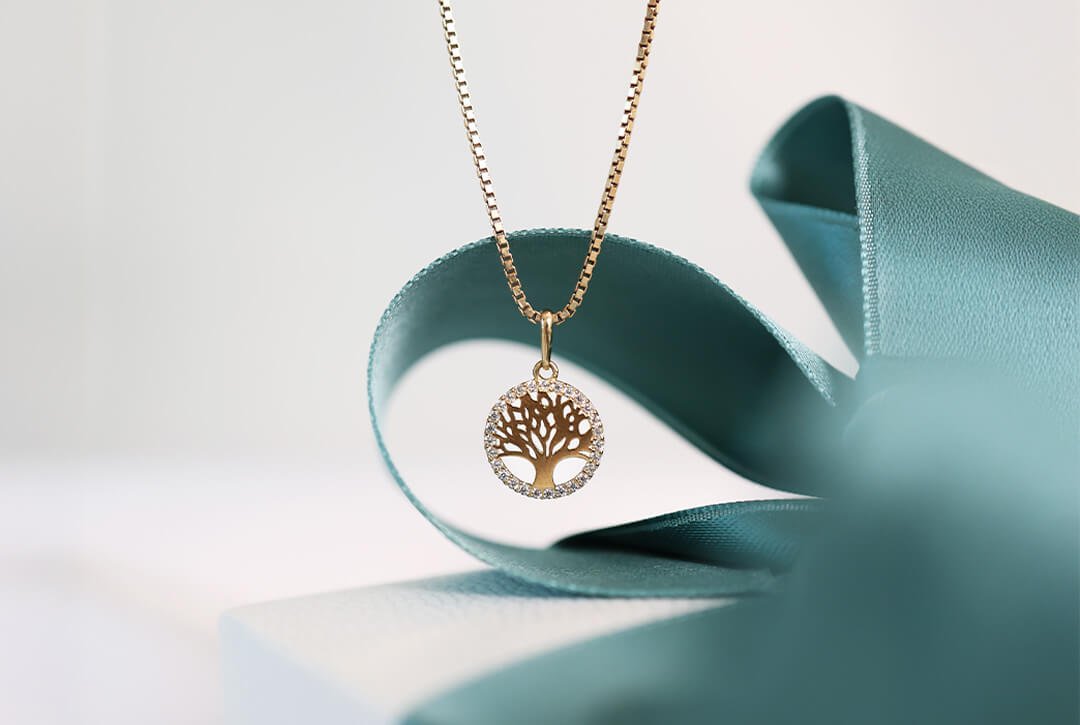 Livets tre-smykker Gullhalskjede med anheng formet som livets tre, plassert på gaveeske med grønt silkebånd.