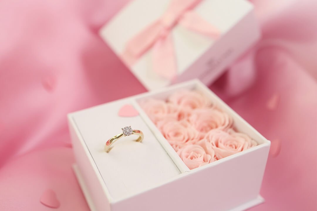 Gaver til henne Gullring med diamant i gaveeske dekorert med små rosa roser og silkebånd på rosa bakgrunn.