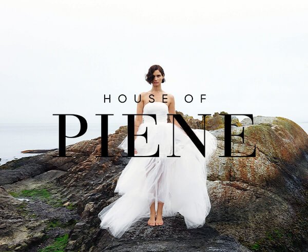 Kvinne i hvit brudekjole står barfot på svaberg ved havet med teksten "House of Piene" over motivet, fotografert forfra.