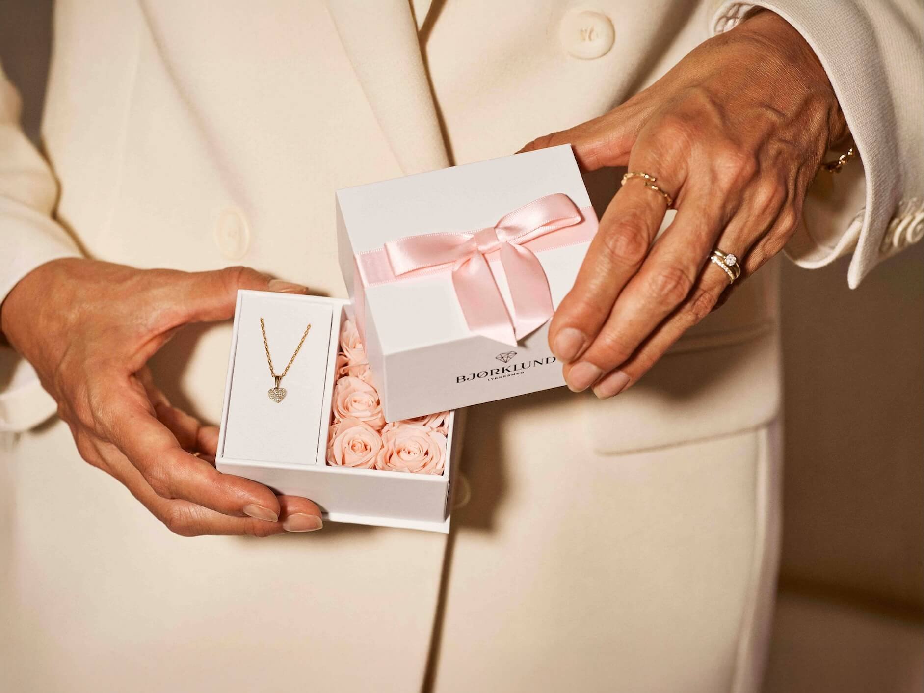 Gaveeske til mamma En kvinne med rosa ballkjole holder en hvit gaveeske med rosa bånd, med rosa blomster og en ring inni.