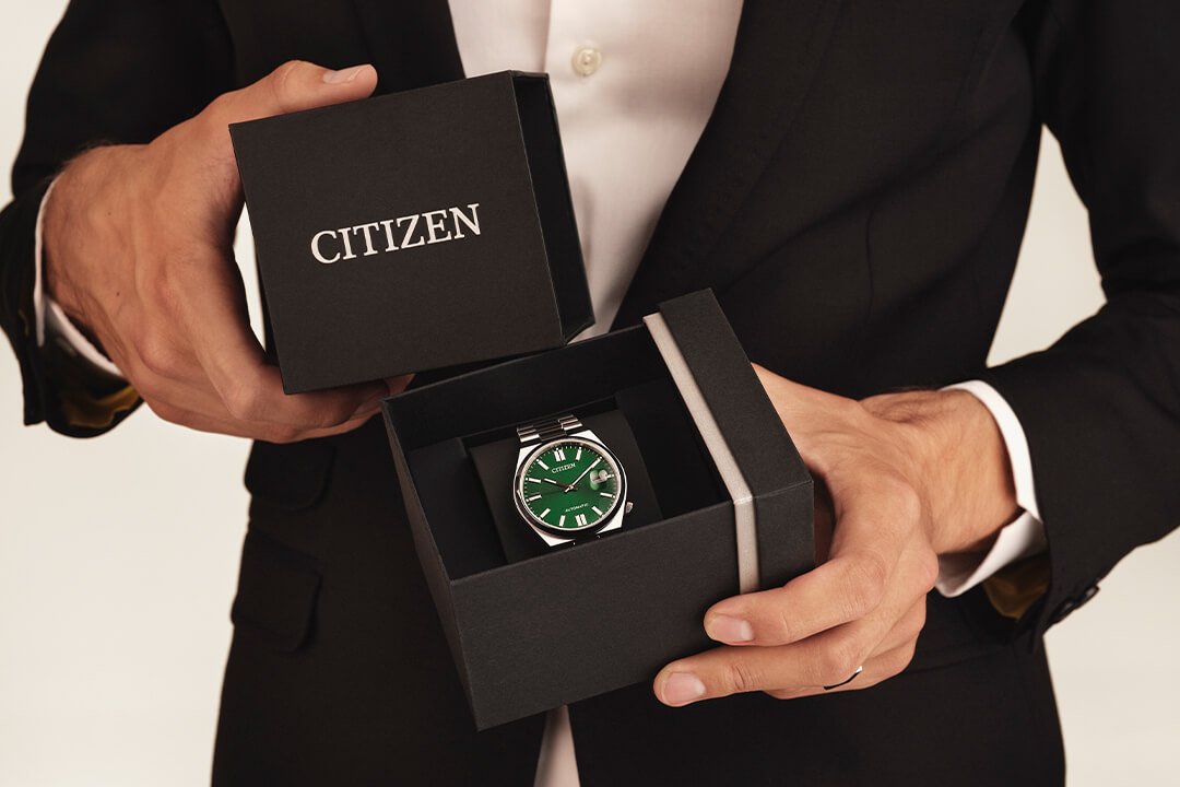 Nærbilde av en mann i sort findress og hvit skjorte som åpner en sort gaveeske med en klokke i fra Citizen.