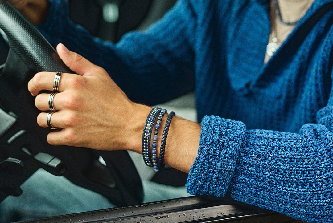 Nærbilde av fanget til en mann med jeans og svart skinnjakke, som holder hendene sine og viser frem sitt armbånd i sølv.