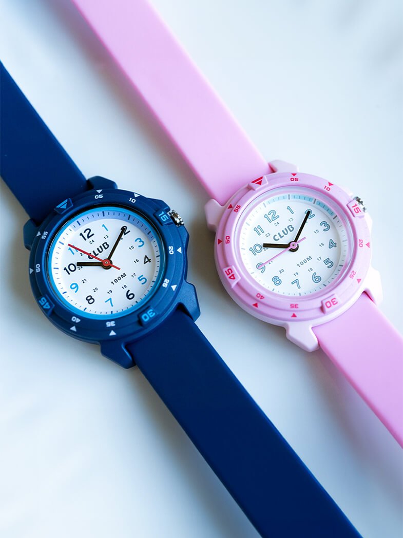 To barneklokker ligger ved siden av hverandre, én blå og én rosa, med hvit urskive, tydelige tall og silikonrem.