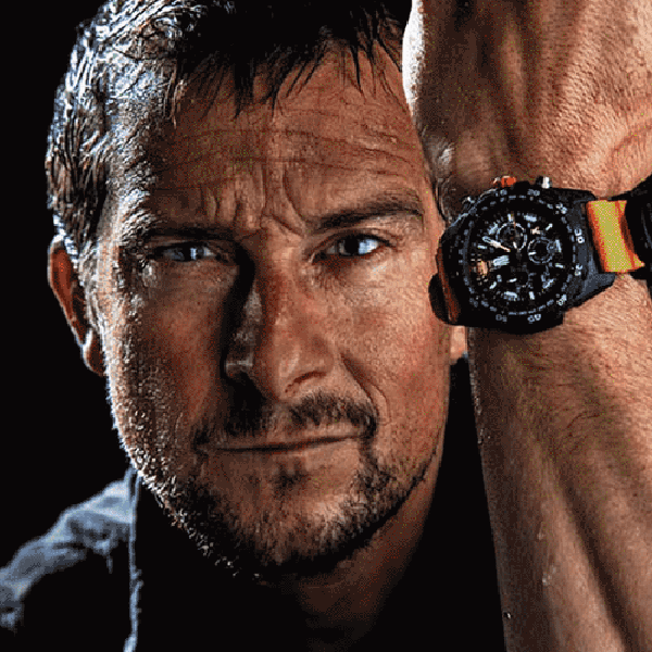 Nært bilde av ansiktet til friluftsentusiasten Bear Grylls som holder opp armen med en sporty Luminox-klokke på håndleddet.