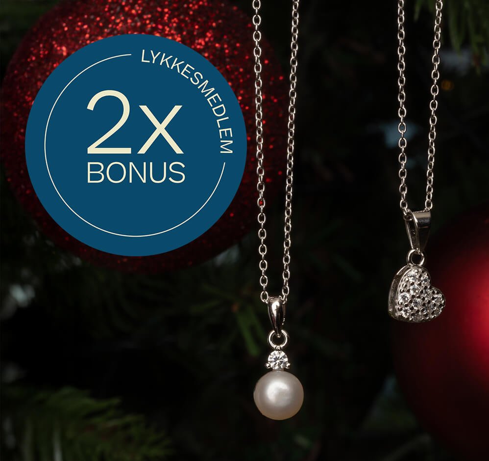 To sølvkjeder med perle- og hjerteanheng henger foran juletre med røde kuler, med blå sirkeltekst «Lykkesmedlem 2x bonus».