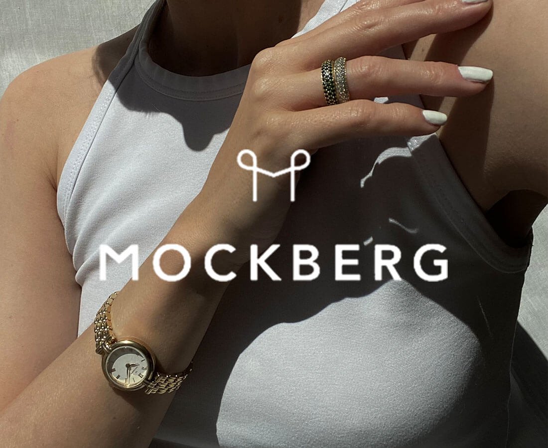 Nærbilde av kvinne med hvit topp som bærer en gyllen Mockberg-klokke og ringer, med logoen over motivet.