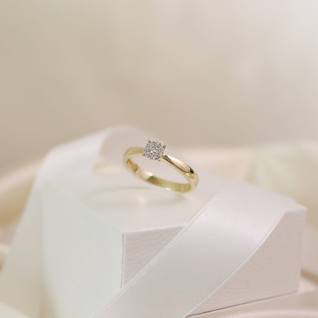 Gullring med diamant står på en hvit gaveeske med satengbånd i lys og myk bakgrunn.