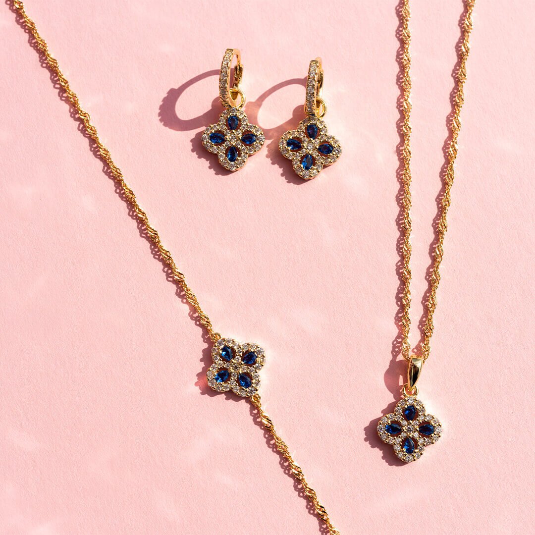 Grønne firkløver-smykker som halsbånd, armbånd og øredobber, på rosa bakgrunn.